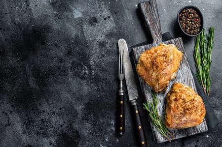 Spicy Bbq grilled chicken thighs on a wooden board with rosemary. Black background. Top View. Copy spaceの写真素材