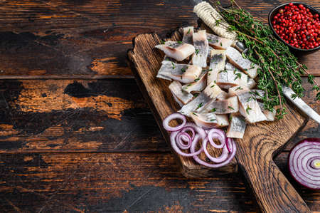 Salted herring fish sliced fillet on a wooden board with thyme. Dark wooden background. Top view. Copy spaceの写真素材