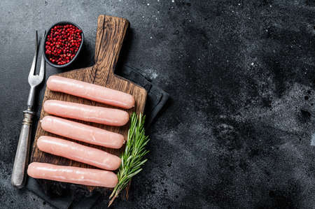 Fresh Raw chicken and turkey meat sausages on a wooden board with rosemary. Black background. Top view. Copy spaceの写真素材