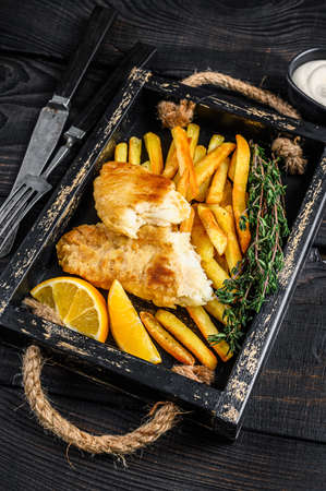 Battered Fish and chips dish with french fries and tartar sauce in a wooden tray. Black wooden background. Top viewの写真素材