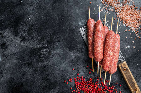 Raw lula or kofta kebabs skewers on a butcher cleaver with salt and pepper. Black background. Top view. Copy spaceの写真素材