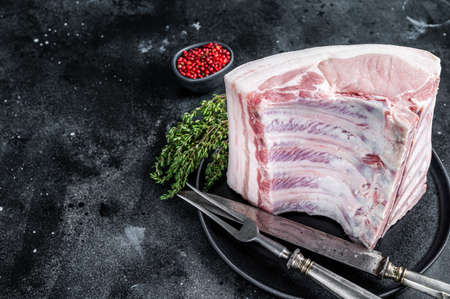 Fresh Raw whole rack of pork loin chops with ribs on a plate with meat fork. Black background. Top view. Copy spaceの写真素材
