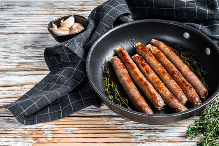 Fried beef and pork meat sausage in a pan with italian herbs and cheese. White wooden background. Top view. Copy spaceの写真素材