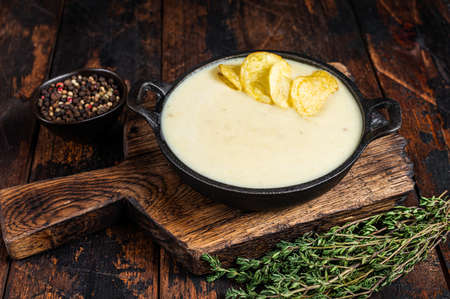 Potato cream soup with potato chips in pan on wooden board. Dark wooden background. Top viewの写真素材