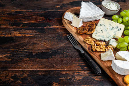 Assorted Cheese board with Brie, Camembert, Roquefort, parmesan, blue cream cheese, grape and nuts. Dark wooden background. Top view. Copy spaceの写真素材