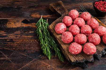 Uncooked Raw meatballs from ground beef and pork meat with rosemary. Dark Wooden background. Top view. Copy spaceの写真素材