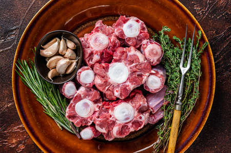 Fresh uncooked beef Oxtail cut Meat on rustic plate with herbs. Dark background. Top viewの写真素材