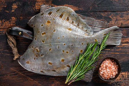 Raw plaice flatfish fish on butcher board with knife. Dark wooden background. Top viewの写真素材