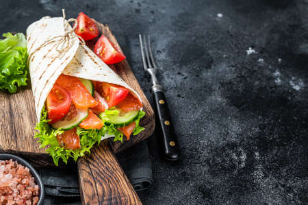 Tortilla Wrap salmon roll with salad, vegetables. Black background. Top view. Copy spaceの写真素材