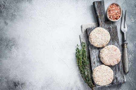 Raw meat patty cutlets with breadcrumbs on wooden cutting board. White background. Top view. Copy...