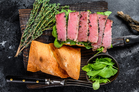 Baguette Tuna steak sandwich with arugula on a cutting board. Black background. Top viewの写真素材
