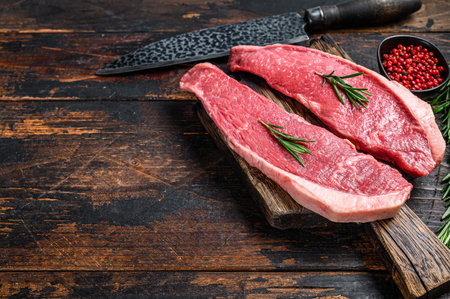 Raw beef meat cap sirloin steak on a cutting board. Dark wooden background. Top view. Copy spaceの写真素材
