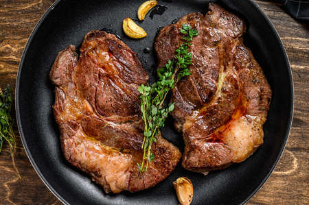 Roasted rib eye steaks in a pan. Dark wooden background. Top viewの写真素材