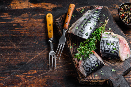 Cut smoked mackerel fish with herbs. Dark wooden background. Top view. Copy spaceの写真素材