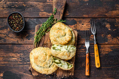 Baked spiral filo pastry puff with feta cheese and spinach. Dark wooden background. Top view