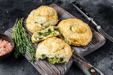 Baked Spanakopita spiral filo pastry puff pie with feta cheese and spinach. Black background. Top...