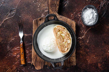 Apfelstrudel strudel with cinnamon, powdered sugar and vanilla ice cream in a pan. Dark background. Top viewの写真素材