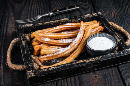 Churros fried sticks with sugar powder in wooden tray. Black background. Top viewの写真素材