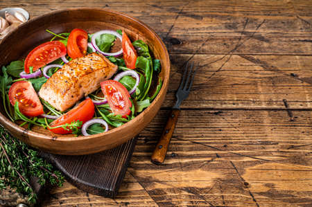 Salmon steak salad with green leaves arugula, avocado and tomato in a wooden plate. Wooden background. Top view. Copy spaceの写真素材