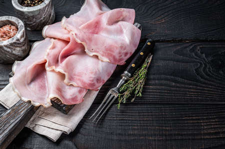 Sliced prosciutto ham on wooden board with herbs. Black wooden background. Top view. Copy spaceの写真素材