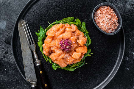 Raw Salmon tartare or tartar with red onion, arugula and capers in black plate. Black background. Top Viewの写真素材