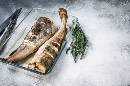 Fish dish - roasted cod fish with herbs in baking dish. White background. Top view. Copy space