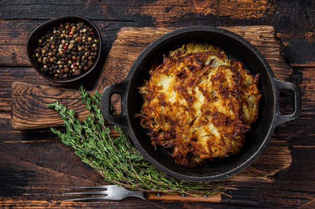 Fried Potato pancakes or Fritters with herbs in a pan. Dark wooden background. Top viewの写真素材