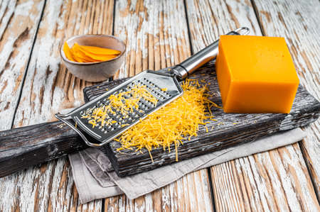 Grated Cheddar Cheese on a wooden cutting board. White wooden background. Top viewの写真素材
