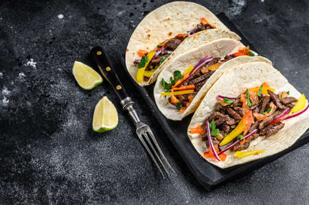 Mexican tacos shells with beef meat, onion, tomato and sweet pepper. Black background. Top view. Copy space
