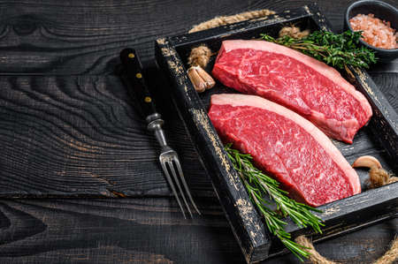 Raw brazilian picanha steak or top sirloin beef meat steak in a wooden tray. Black wooden background. Top view. Copy spaceの写真素材