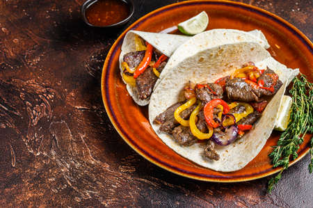Fajitas Tortilla wraps with beef meat steak stripes, sweet pepper and onions. Dark Wooden background. Top view. Copy spaceの写真素材