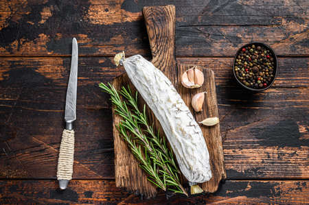 Spanish dry cured salchichon salami on a cutting board. Dark wooden background. Top view