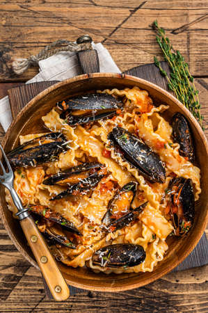 Mussels and clams Mafaldine pasta with tomato sauce in a rustic wooden plate. Wooden background. Top viewの写真素材