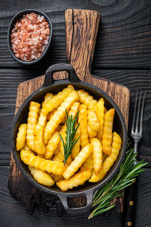 Fried Crinkle French fries potatoes in a pan. Black Wooden background. Top viewの写真素材