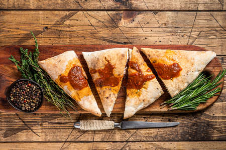 Cut and sliced Calzone closed pizza with ham and cheese on wooden board with hot tomato sauce....