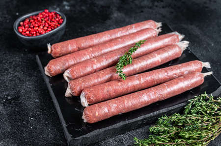 Fresh Raw butchers sausages in skins with thyme on marble board. Black background. Top viewの写真素材