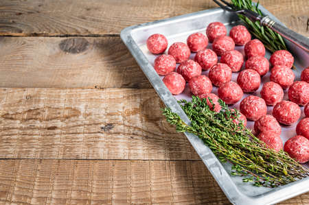 Recipe for cooking meatballs from ground beef with thyme and rosemary in kitchen tray. Wooden background. Top view. Copy spaceの写真素材