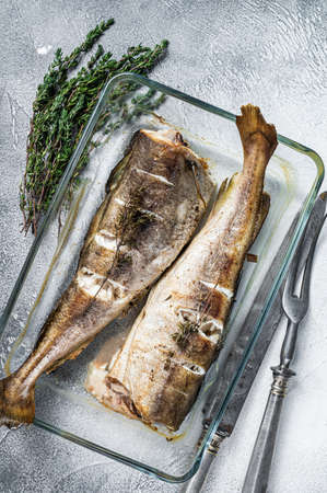 Fish dish - roasted cod fish with herbs in baking dish. White background. Top view