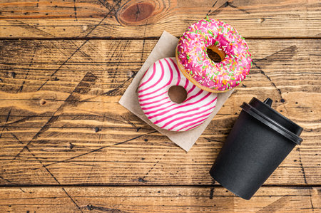 Pink glazed donuts on a kitchen table with coffee. Wooden background. Top view. Copy spaceの写真素材