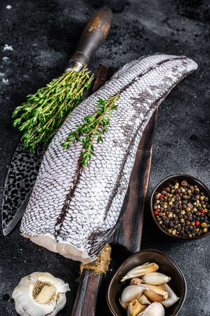 Raw grenadier macrurus white fish on a wooden cutting board. Black background. Top view