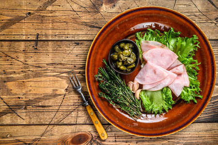Sliced smoked ham with fresh salad and capers on a plate. wooden background. Top view. Copy spaceの写真素材