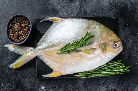 Raw fish pompano with herbs on a marble board. Black background. Top viewの写真素材
