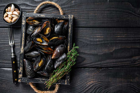 Steamed Mussels in shells in a wooden tray with herbs. Black wooden background. Top view. Copy spaceの写真素材