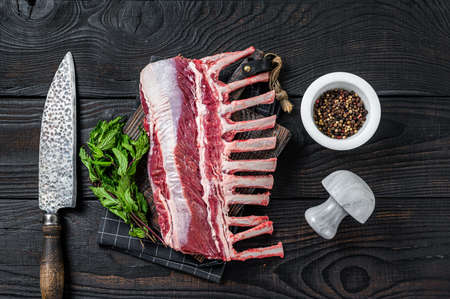 Rack of lamb ready for cooking on a butcher cutting board. Black background. Top viewの写真素材