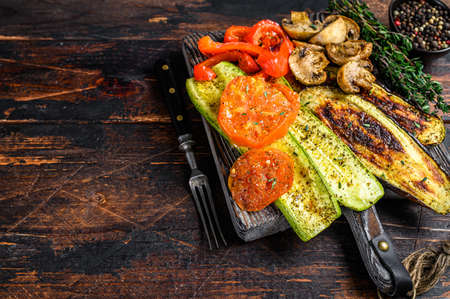 Grilled vegetables bell pepper, zucchini, eggplant and tomato with dry herbs on a wooden board. Dark wooden background. Top view. Copy spaceの写真素材