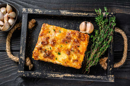 Portion of Lasagna with mince beef meat and tomato bolognese sauce in a wooden tray. Black wooden background. Top viewの写真素材