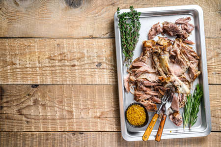 Baked pork knuckle eisbein meat on a baking pan with herbs. Wooden background. Top view. Copy space