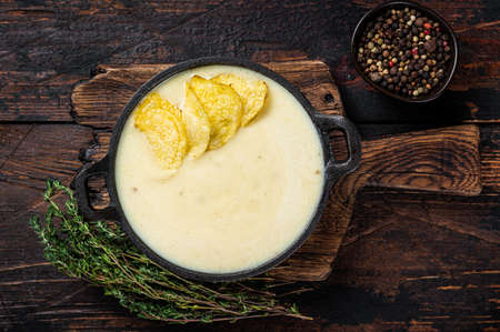 Potato cream soup with potato chips in pan on wooden board. Dark wooden background. Top viewの写真素材