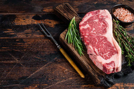 Raw new york strip beef steak or striploin on a wooden board. Dark wooden background. Top view. Copy spaceの写真素材