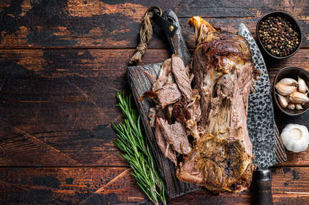 Baked lamb mutton cutting shoulder meat on a wooden board. Dark wooden background. Top view. Copy spaceの写真素材